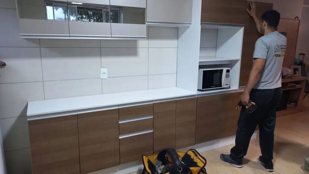Montador de móveis instalando armário aéreo de cozinha com nível preciso.